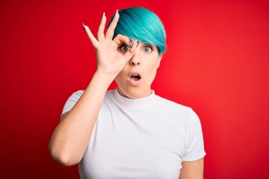 Mavi saçlı, kırmızı arka planda sıradan tişörtler giyen, şaşırmış yüzüyle şaşırmış, parmaklarından bakan genç, güzel bir kadın. İnançsız ifade.