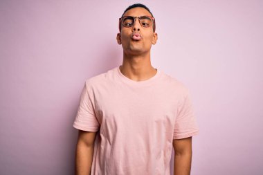 Yakışıklı Afro-Amerikan erkeği pembe arka planda günlük tişört ve gözlük takıyor dudaklarıyla balık suratı yapıyor, çılgınca ve komik bir jest. Komik ifade.