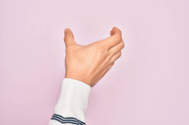 Kafkasyalı genç adam parmaklarını pembe arka planda gösteriyor. Görünmez bir nesne tutuyor, eli boş, kesiyor ve kapıyor.