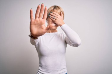 Modern kısa saç stiline sahip genç, sarışın bir kadın izole edilmiş arka planda duruyor gözleri ellerle örtüyor ve üzgün ve korku ifadeleriyle hareketlerini durduruyor. Utanç verici ve olumsuz bir kavram..