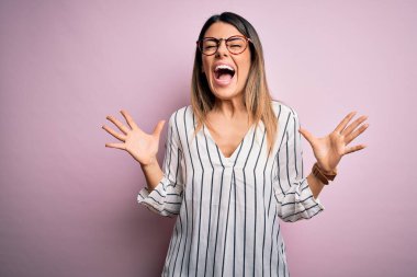 Pembe arka planda rahat çizgili tişört ve gözlük takan genç ve güzel bir kadın başarıyı kutluyor. Kolları havada ve gözleri kapalı bağırıyor. Heyecanlı. Kazanan konsept