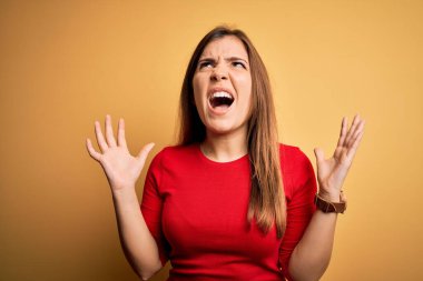 Güzel genç bir kadın, sarı üzerine gündelik kırmızı tişört giyip izole edilmiş arka plan deliliği ve kızgınlığı agresif bir ifade ve kollarla bağırış çağırış. Hayal kırıklığı konsepti.