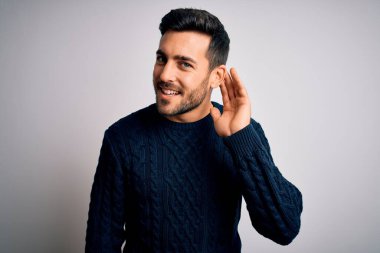 Sakallı, sıradan bir süveter giyen, beyaz arka planda dikilen, ağzı kulaklarında, dedikoduları ve dedikoduları dinleyen genç yakışıklı bir adam. Sağırlık kavramı.