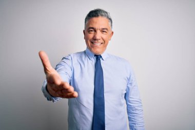 Orta yaşlı, yakışıklı, gri saçlı, şık gömlekli ve kravatlı bir iş adamı. Dostça bir selamlama ve hoş geldin hediyesi olarak gülümsüyor. Başarılı bir iş..