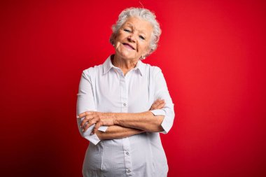 Soyutlanmış kırmızı arka planda duran zarif tişört giyen, kollarını kavuşturup kameraya gülümseyen son derece güzel bir kadın. Pozitif kişi.