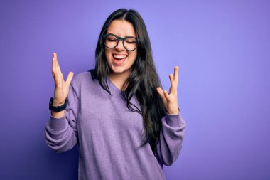 Mor izole edilmiş arka planda gözlük takan genç esmer kadın başarının çılgınlığını kollarını kaldırarak ve gözlerini kapatarak kutluyor. Heyecanlı çığlık atıyor. Kazanan konsept