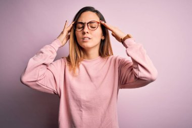 Mavi gözlü güzel sarışın kadın pembe arka planda süveter ve gözlük takıyor. Başında baş ağrısı var çünkü stres var. Migren ağrısı..