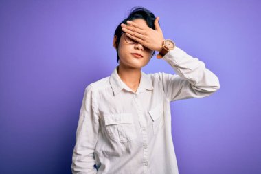 Genç, güzel Asyalı bir kız. Günlük gömlek ve gözlük takıyor. Mor arka planda duruyor. Görme, saklama ve reddetme konsepti