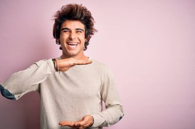 İzole edilmiş pembe arka planda duran, büyük ve büyük beden işareti ve ölçü sembolü gösteren sıradan bir tişört giyen genç yakışıklı bir adam. Kameraya bakıp gülümsüyor. Ölçüm konsepti.