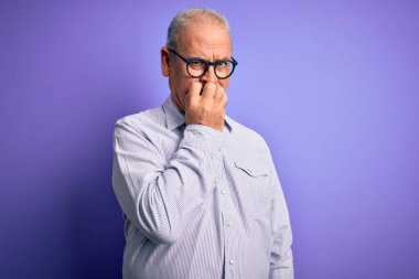 Mor arka planda çizgili gömlek ve gözlük takan orta yaşlı yakışıklı, gergin ve ağzı tırnak yiyen elleri olan bir adam. Endişe sorunu.