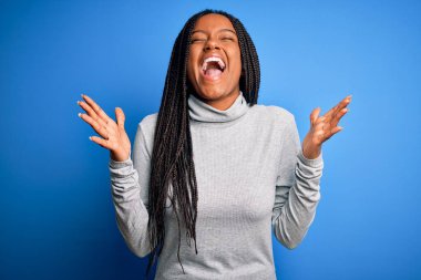 Genç Afro-Amerikalı kadın mavi balıkçı yaka kazak giyip başarıyı kutluyor. Kollarını kaldırmış, gözlerini kapatmış heyecanla haykırıyor. Kazanan konsept