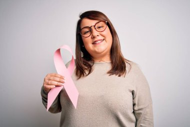 Güzel ve iri bir kadın göğüs kanseri farkındalığını koruyan pembe kurdeleli mutlu bir yüzü olan ve kendine güvenen bir gülümsemeyle dişlerini gösteren bir kadın.