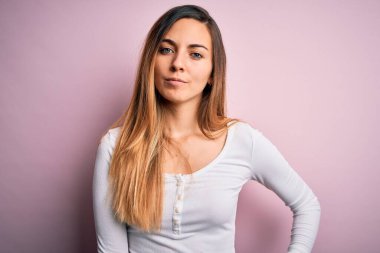 Pembe arka planda beyaz tişört giyen mavi gözlü güzel sarışın kadın yüzünde ciddi bir ifadeyle rahatlamış. Basit ve doğal bir şekilde kameraya bakıyorsun..