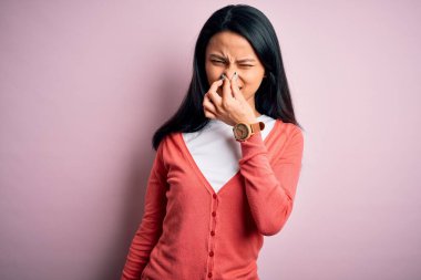 Genç, güzel bir Çinli kadın pembe arka planda rahat bir süveter giyiyor pis ve iğrenç bir koku alıyor, dayanılmaz bir koku, nefesini burnunda tutuyor. Kötü kokuyor.