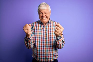 Kolları havada, gözleri kapalı zaferi kutlarken gülümseyen ve başarı için heyecanla karışık mor arka plan üzerinde sıradan bir gömlek giyen kıdemli yakışıklı beyaz adam. Kazanan konsept.