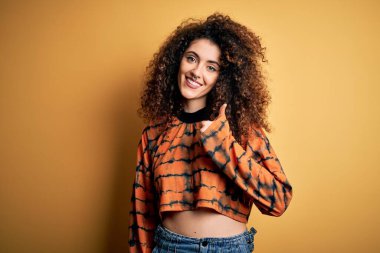 Kıvırcık saçlı, piercingli, sıradan tişörtlü, güzel, esmer bir kadın mutlu baş parmaklarıyla el hareketi yapıyor. Kameraya bakıp başarıyı gösteren ifade onaylanıyor.