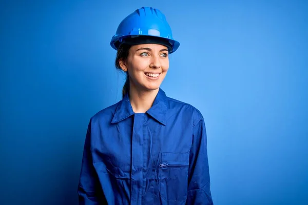青い目をした若い美しい労働者の女性は 顔に笑顔で横に見えるセキュリティヘルメットと制服を着て 自然な表情 自信を持って — ストック写真