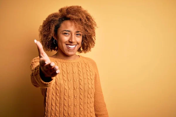 カジュアルなセーターを着て巻き毛を持つ若い美しいアフリカ系アメリカ人アフロ女性は 挨拶や歓迎として握手を提供フレンドリーな笑みを浮かべて 成功事業 — ストック写真