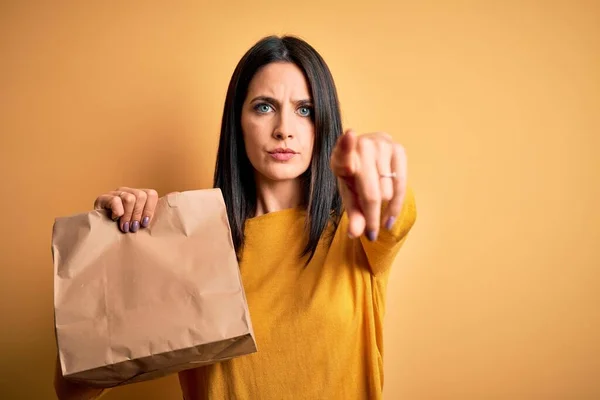 年轻的黑发女人 蓝眼睛 拿着装有食物的纸袋 手指指向相机和你 正面是积极自信的手势 — 图库照片