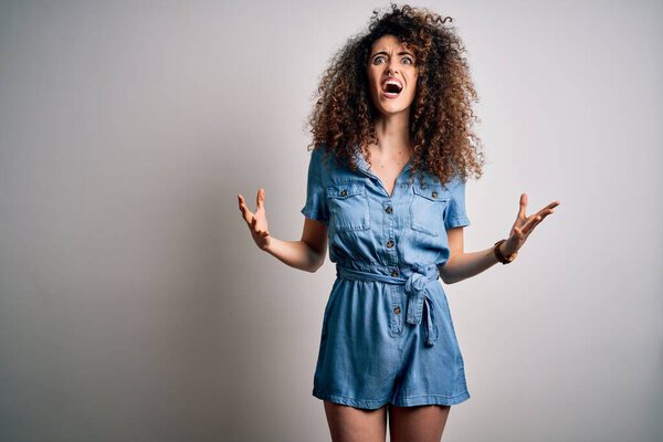 Молодая красивая женщина с вьющимися волосами и пирсинг носить случайные джинсовые платья сумасшедшие и сумасшедшие крики и крики с агрессивным выражением лица и поднятыми руками. Концепция разочарования
.