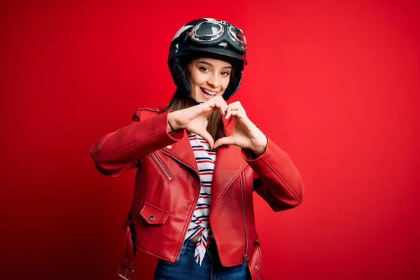 若い美しいブルネットのオートバイのヘルメットと赤いジャケットを身に着けているオートバイの女性は手でハートシンボルの形をして愛に笑みを浮かべている ロマン主義 — ストック写真