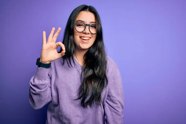 年轻的黑发女人戴着眼镜 带着紫色孤立的背景 微笑着 手指手画脚地签了名 成功表达 — 图库照片