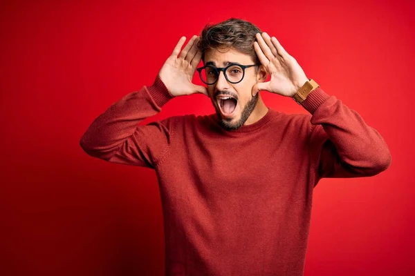 Sakallı Gözlüklü Süveterli Genç Bir Adam Kırmızı Arka Planda Dikilirken — Stok fotoğraf