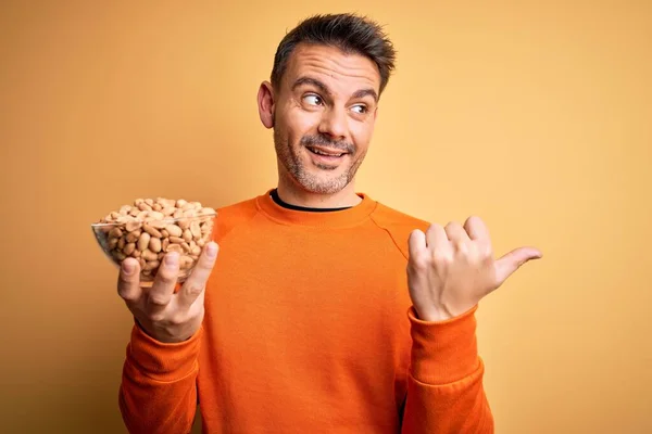 Jovem Homem Bonito Segurando Tigela Com Amendoins Sobre Fundo Amarelo — Fotografia de Stock