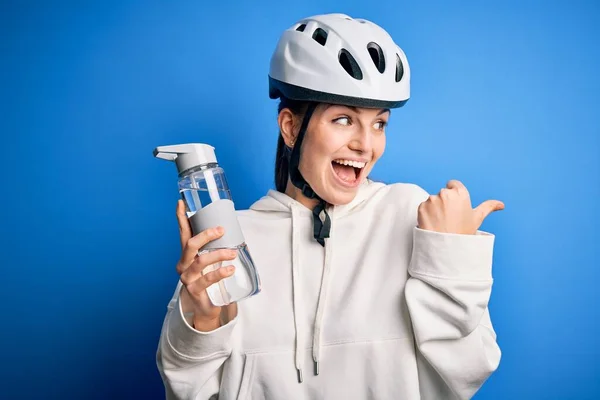 年轻美丽的红头发骑自行车的女人 戴着自行车头盔 喝着瓶装水 手指朝天 笑容满面 — 图库照片