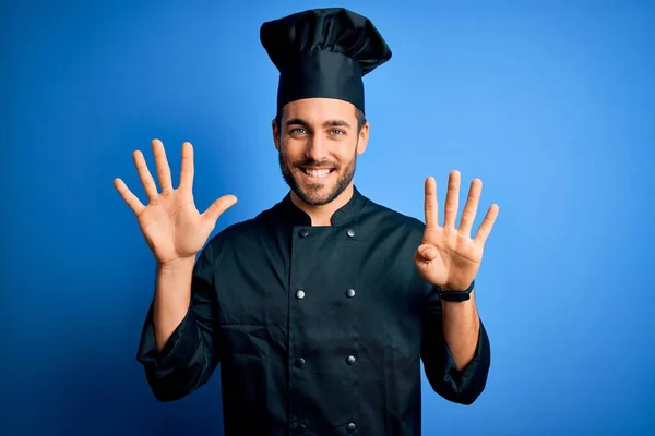 年轻英俊的厨师 留着胡子 身穿炊具制服 头戴蓝色背景的帽子 带着九号手指 面带微笑 自信而快乐 — 图库照片