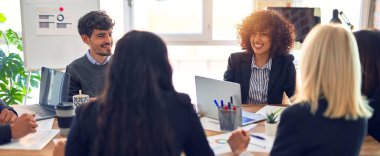 Bir grup iş adamı mutlu ve kendinden emin gülümsüyor. Yüzünde gülümsemeyle çalışmak, dizüstü bilgisayar kullanmak ve ofiste konuşmak.