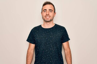 Mavi gözlü, beyaz arka planda mutlu ve havalı bir gülümsemesi olan sıradan tişörtler giyen genç yakışıklı bir adam. Şanslı kişi..