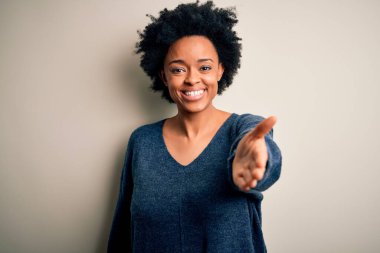 Kıvırcık saçlı, sıradan bir süveter giyen, dostça gülümseyen, selamlaşmak ve selamlamak için tokalaşan güzel Afro-Amerikan bir kadın. Başarılı bir iş..