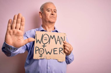 Orta yaşlı, beyaz bir adam kadın hakları için pankart istiyor. Elinde kadın gücü mesajı var. Elinde dur işareti, ciddi ve kendinden emin bir ifade var.