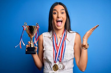 Genç ve güzel esmer başarılı kadın, elinde madalyalar, çok mutlu ve heyecanlı, kazanan yüz ifadesi zaferi büyük bir gülümsemeyle kutluyor ve ellerini kaldırıyor.