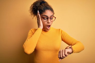 Sarı arka planda süveter ve gözlük takan Afro-Amerikan genç güzel bir kız. Endişeli saate bakıyor, geç kalmaktan korkuyor.