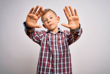 Mavi gözlü, zarif gömlekli küçük beyaz çocuk izole arka planda duruyor. El ve parmakları kullanarak çerçeve yapıyor. Kamera perspektifi kullanıyor.