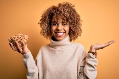 Kıvırcık saçlı, sağlıklı fıstıklı genç Afro-Amerikalı kadın. Çok mutlu ve heyecanlı. Kazanan ifade zaferi büyük bir gülümsemeyle ve el kaldırarak kutluyor.