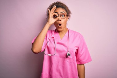Afro-Amerikalı hemşire kız tıbbi üniforma giyiyor ve pembe arka planda steteskop takıyor. Şok olmuş bir jest yapıyor. İnançsız ifade.