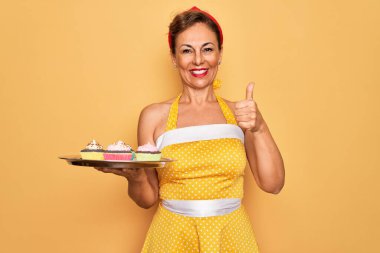 Orta yaşlı bir kadın 50 'lerin stili retro elbise tepsisi içinde kek tepsisi ve kocaman gülümsemesi olan tamam işareti yapan, parmaklarıyla başparmağını kaldıran mükemmel bir işaret.