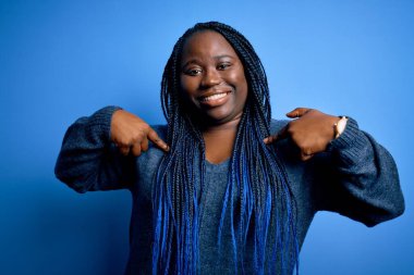 Mavi arka planda normal süveter giyen, kendine güvenen, gururlu ve mutlu parmakları olan Afro-amerikalı kadın..