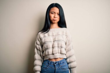 İzole edilmiş beyaz arka plan üzerine gündelik kazak giyen genç, güzel Çinli kadın depresyonda ve endişe içinde, kızgın ve korkmuş. Üzücü ifade.