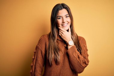 İzole edilmiş sarı arka plan üzerinde duran sıradan süveter giyen genç ve güzel bir kız kameraya bakarak kollarını kavuşturup, ellerini çenesine kaldırarak gülümsüyor. Olumlu düşünüyorum..