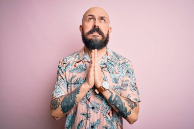 Sakallı ve dövmeli yakışıklı, pembe arka planda sıradan bir çiçek gömleği giyen, elleri bağlı, yalvaran ve dua eden, yüzünde umut ifadesi olan çok duygusal ve endişeli bir adam. Yalvarıyorum..