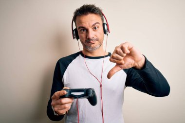 Oyun oynayan yakışıklı oyuncu, joystick ve kulaklık kullanıyor. Kızgın yüzlü, negatif işaretli, başparmakları aşağıda, reddedilme kavramından hoşlanmadığını gösteriyor.