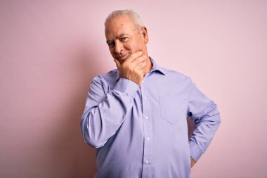 Orta yaşlı, beyaz gömlekli, pembe arka planda duran, kolları çapraz ve çenesi açık bir şekilde kameraya gülümseyen yakışıklı bir adam. Olumlu düşünüyorum..