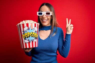 Üç boyutlu gözlük takan ve patlamış mısır yiyen genç bir kadın sinemada gülümseyen bir film izliyor parmaklarını zafer işareti yaparken gösteren kameraya bakıyor. İki numara..