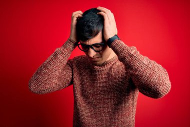Kırmızı arka planda inek gözlüğü takan genç yakışıklı İspanyol adam acı ve migren yüzünden çaresiz ve stresli bir baş ağrısı çekiyor. Ellerini başının üstüne koy..