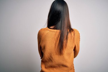 Genç, güzel esmer kadın, izole edilmiş beyaz arka plan üzerine gündelik bir kazak giyip kollarını kavuşturup geriye bakıyor.