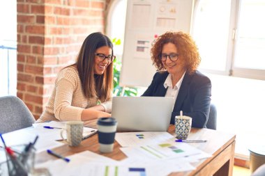 Two beautiful businesswomen smiling happy and confident. Sitting with smile on face working together using laptop at the office